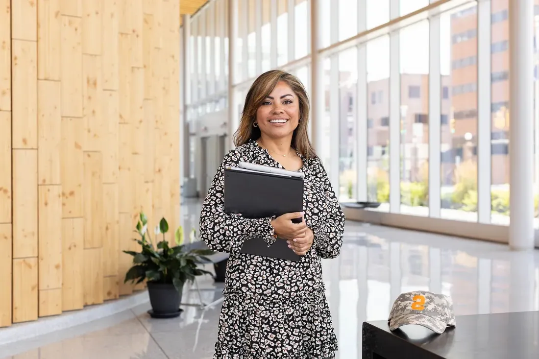 Person holding books while standing and smiling.